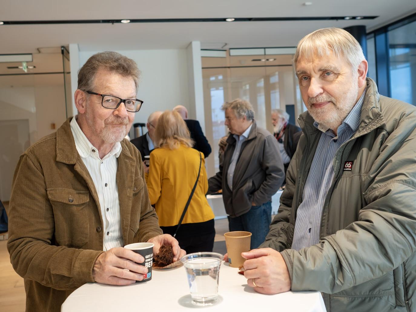 Tveir menn við hátt borð brosa við ljósmyndara.