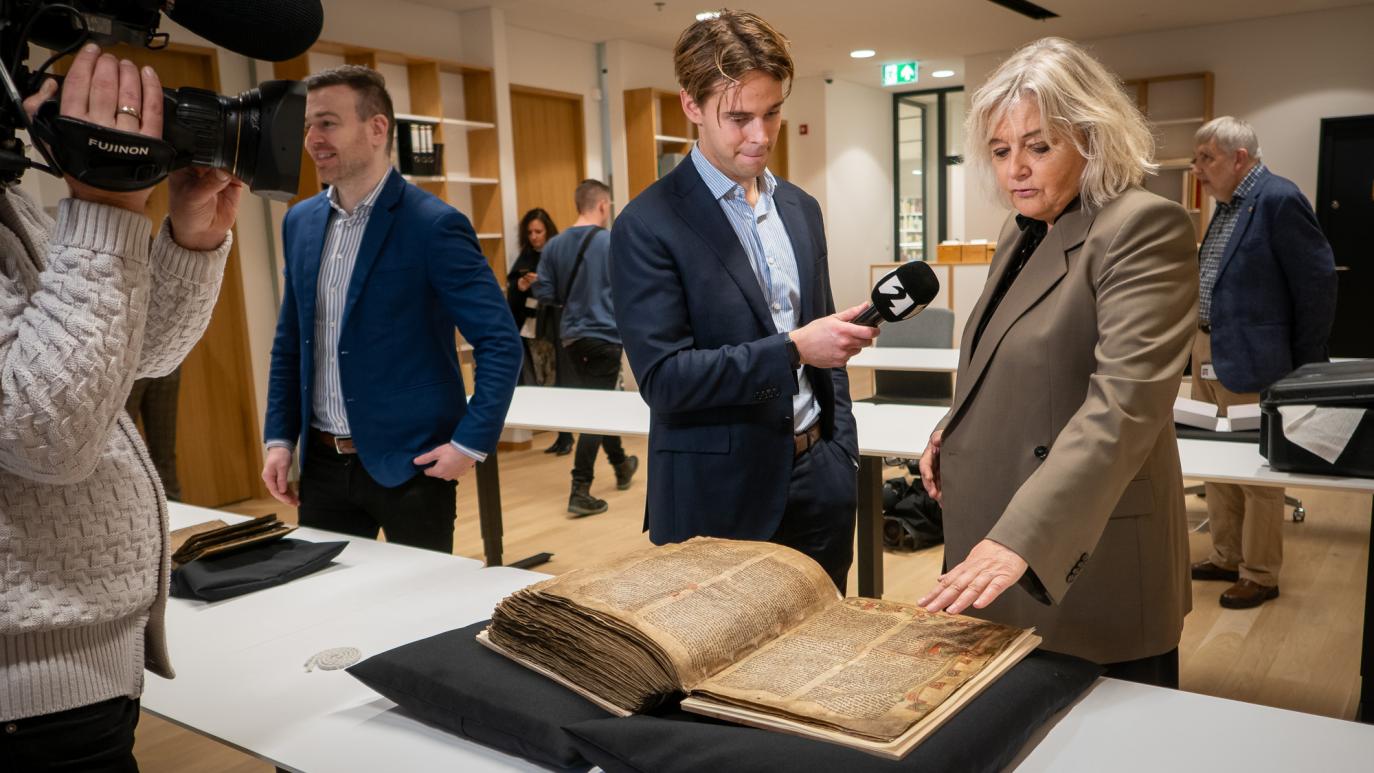 Kona bendir á stað á handriti og ræðir við fjölmiðlamann sem stendur við hlið hennar.